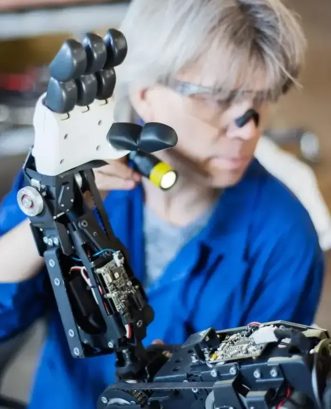 Engineer inspecting and assembling a robotic hand with exposed electronics in a robotics automation lab, representing robotics engineering and automation expertise.